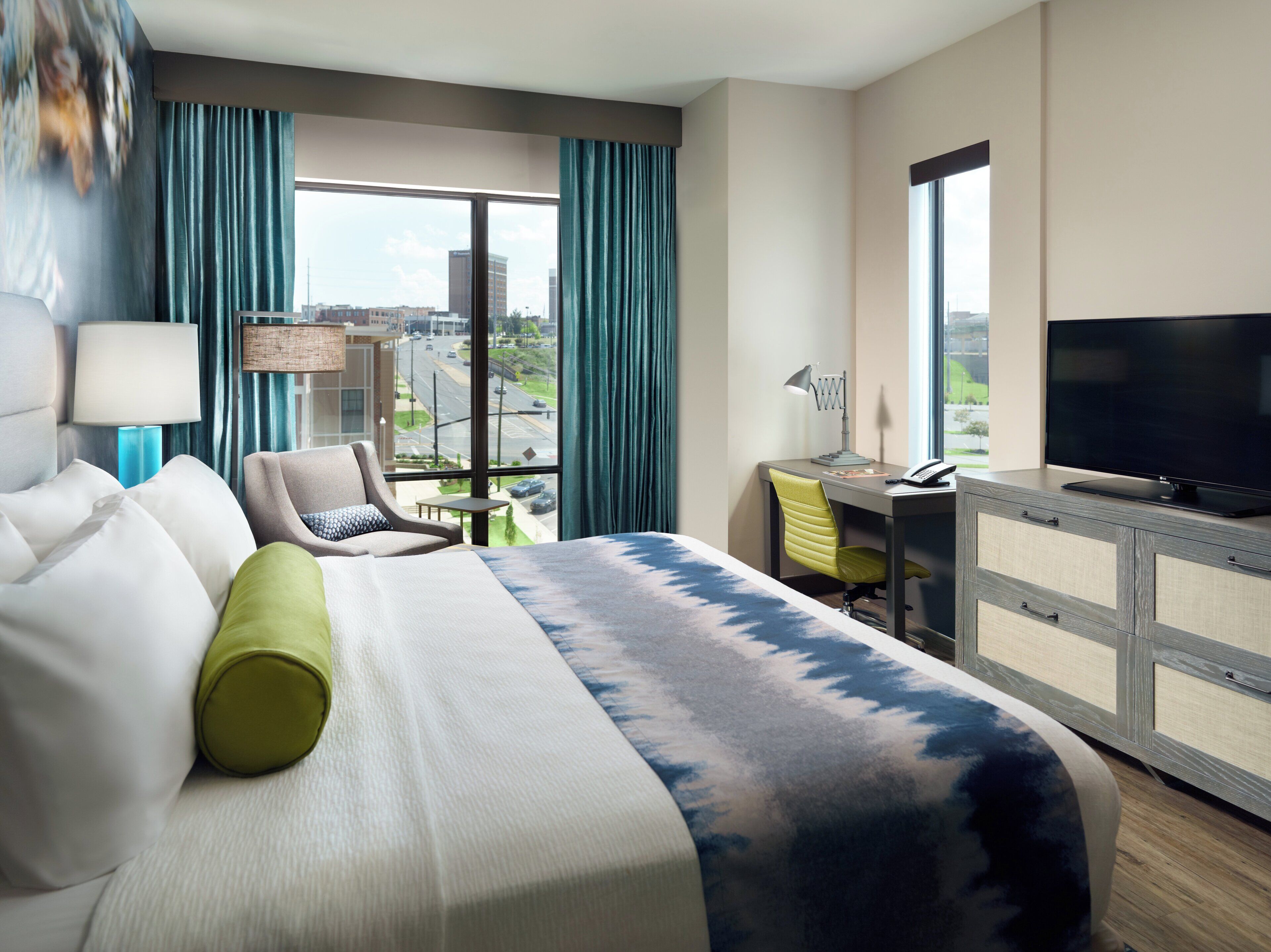 Une chambre d’hôtel équipée d’un lit, d’un bureau, d’une chaise, d’une télévision et offrant une vue sur le paysage urbain.