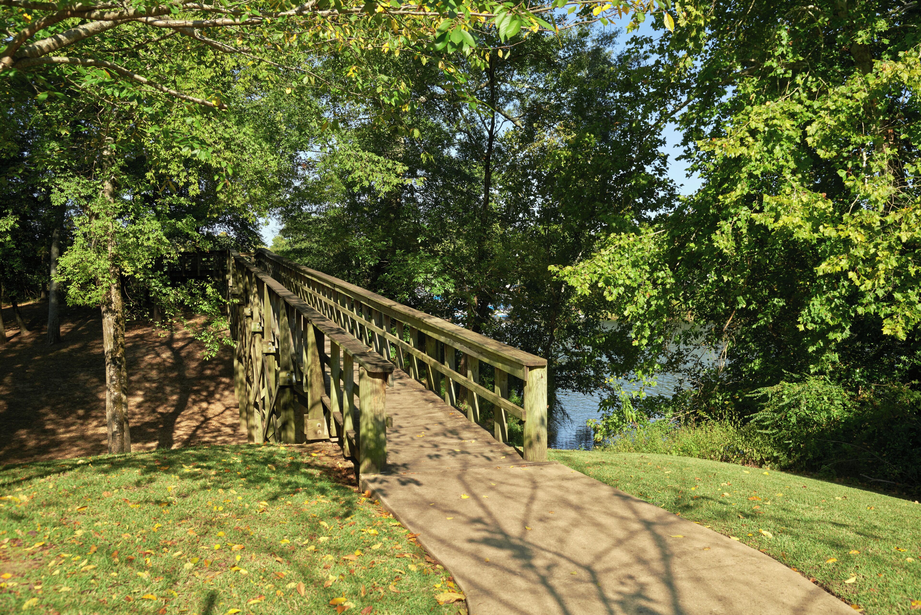 A wooden bridge over a body of water, surrounded by trees and grass.