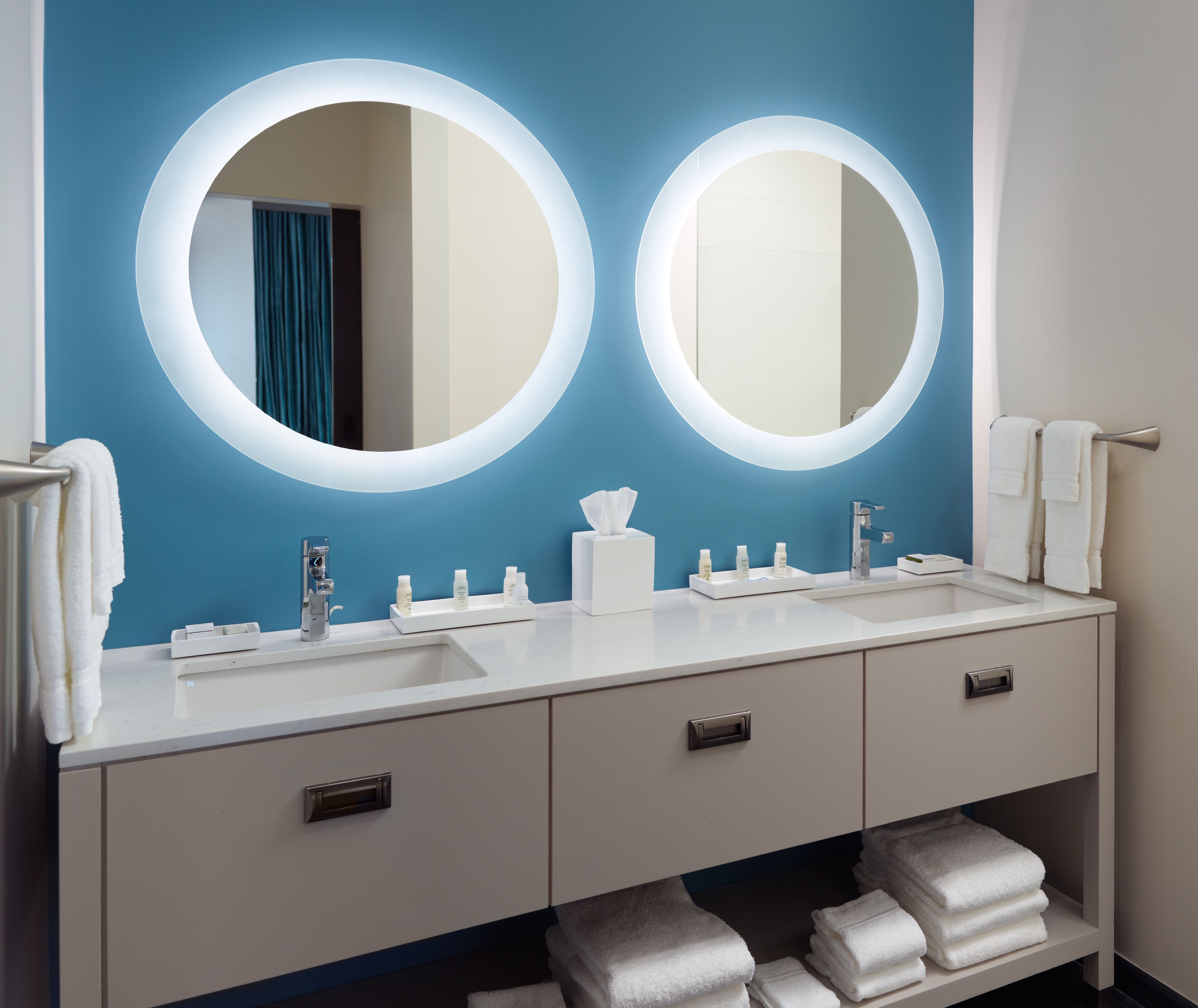 Un baño moderno con dos espejos redondos, un lavabo blanco y un mueble de tocador con cajones.