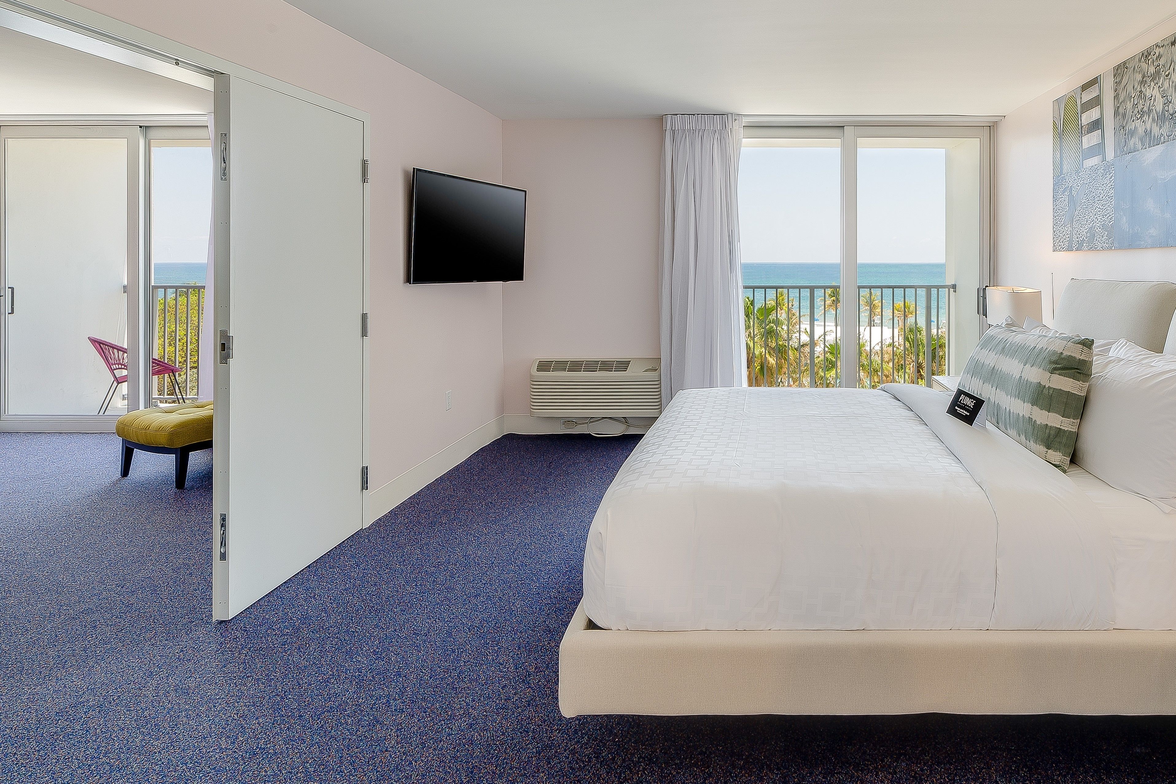 Habitación de hotel con cama, televisor de pantalla plana, balcón con vista al mar y una silla.