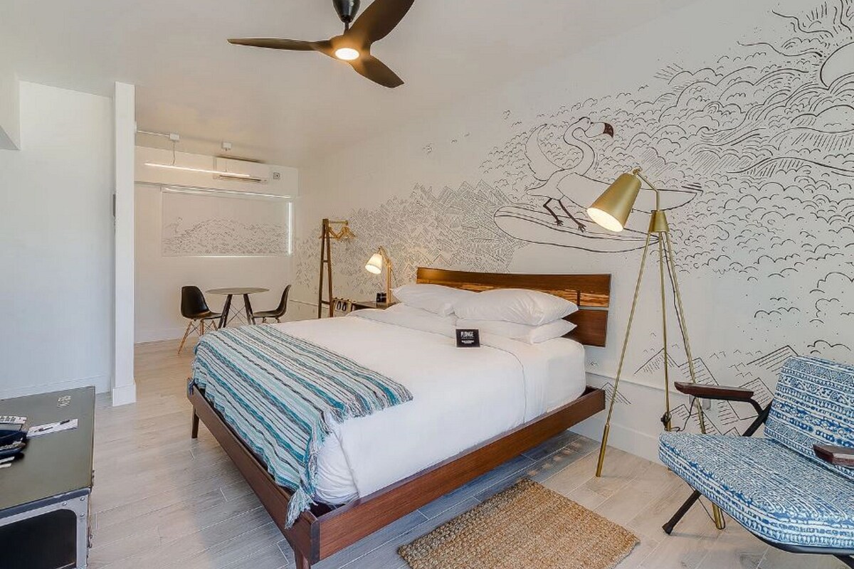 A bedroom with a bed, a desk, a chair, a standing lamp, and a ceiling fan.