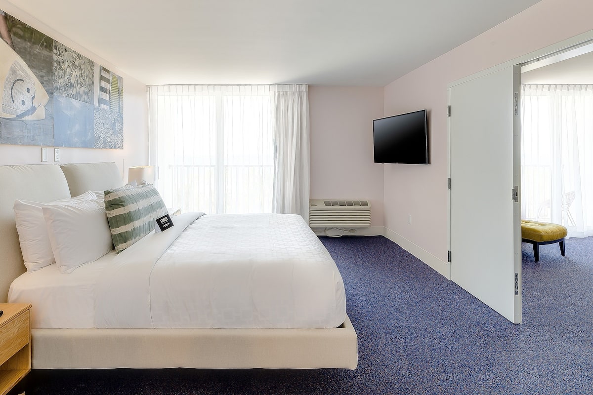 A hotel room with a large bed, a flat-screen TV mounted on the wall, and a sliding door leading to another room.