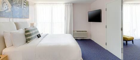 A hotel room with a large bed, a flat-screen TV mounted on the wall, and a sliding door leading to another room.