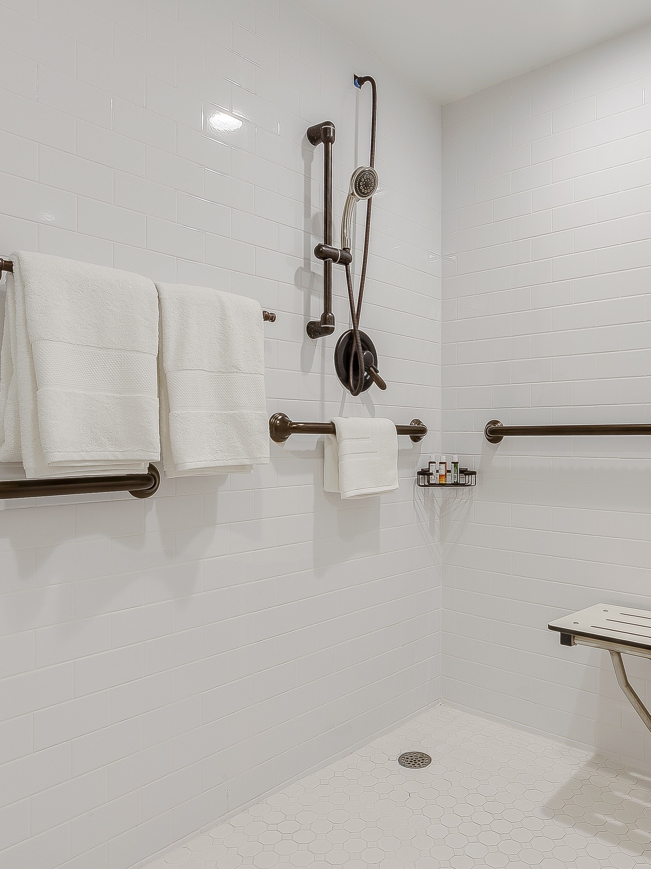 A bathroom with white subway tiles, a shower with a handheld showerhead, and two towel racks with white towels.