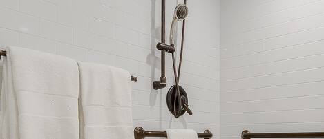 A bathroom with white subway tiles, a shower with a handheld showerhead, and two towel racks with white towels.