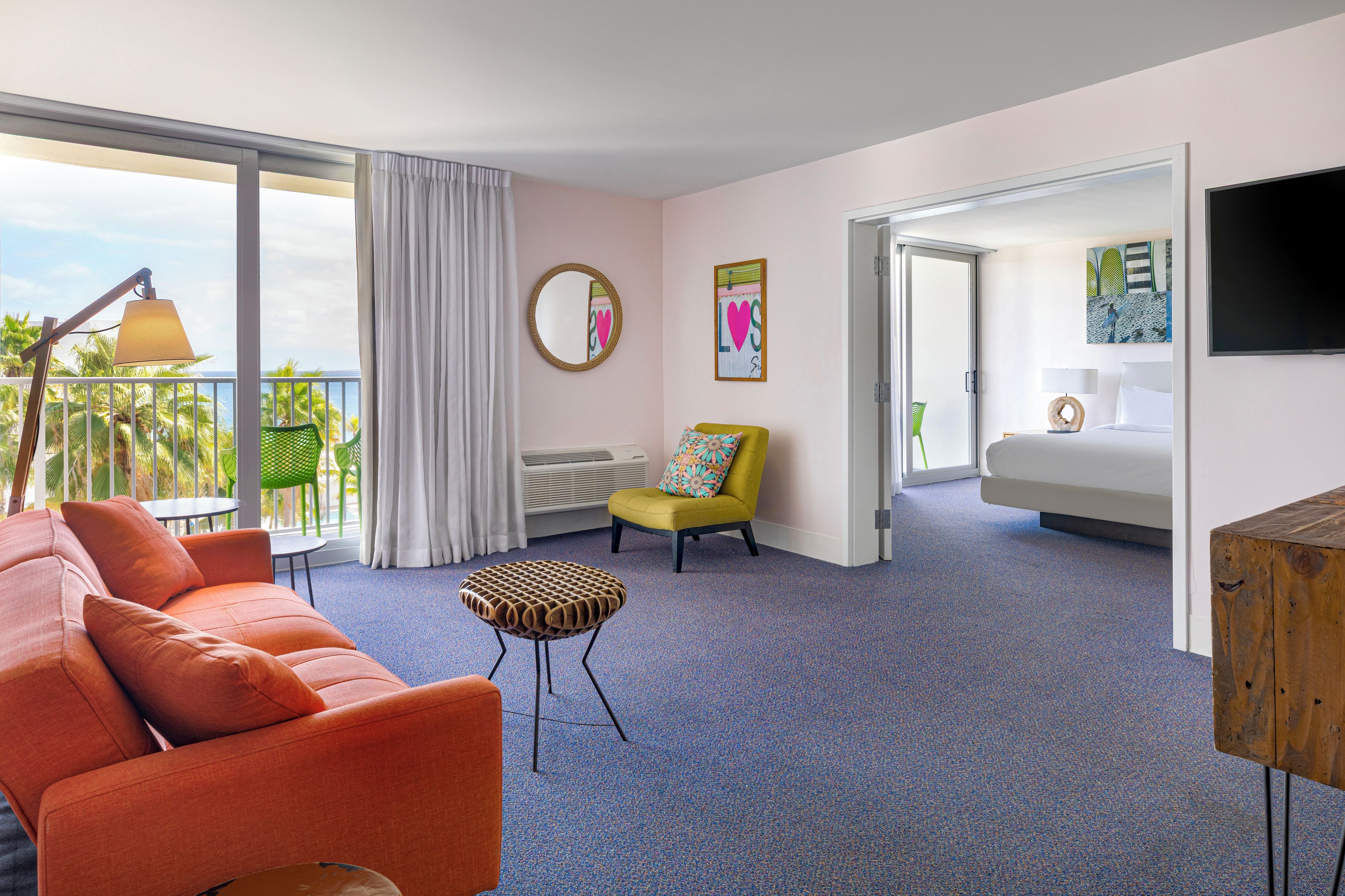 Een hotelkamer met een balkon, een bank, een stoel, een bed en een televisie.