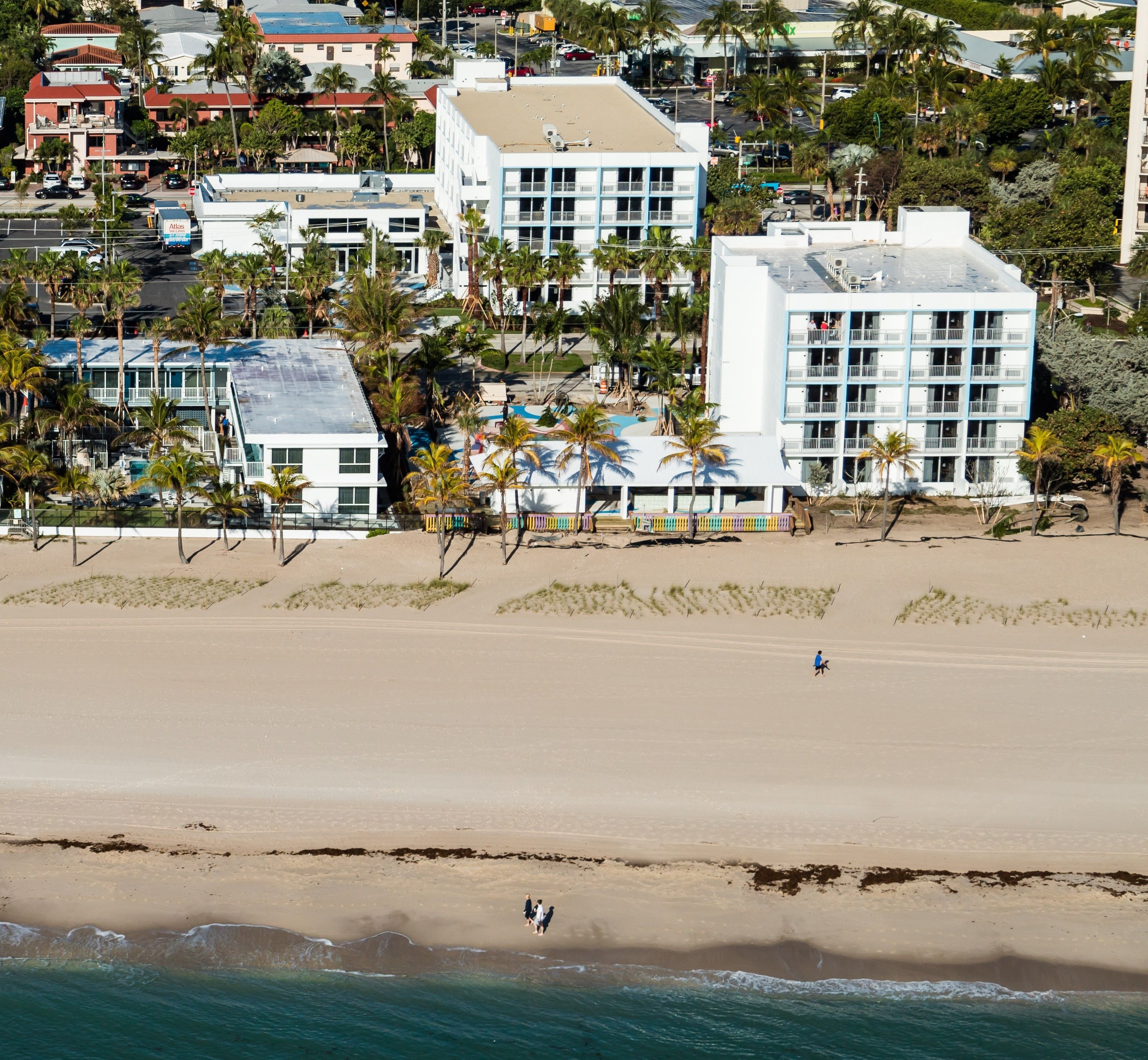 A beachfront hotel with multiple floors, a sandy beach in the foreground, and palm trees in the background.