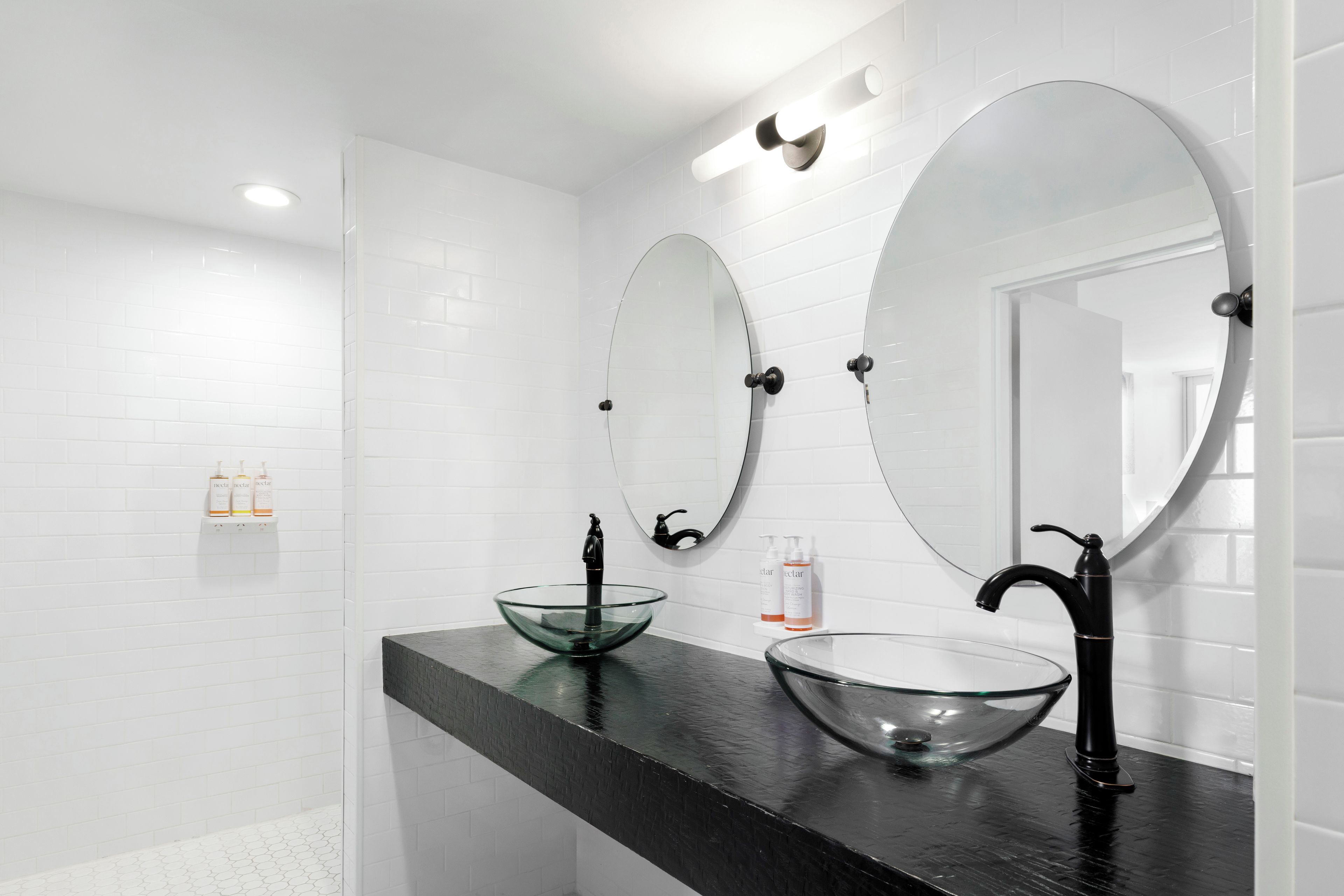 Une salle de bain moderne avec deux grands miroirs, un lavabo en forme de bol en verre et un plan de toilette noir.