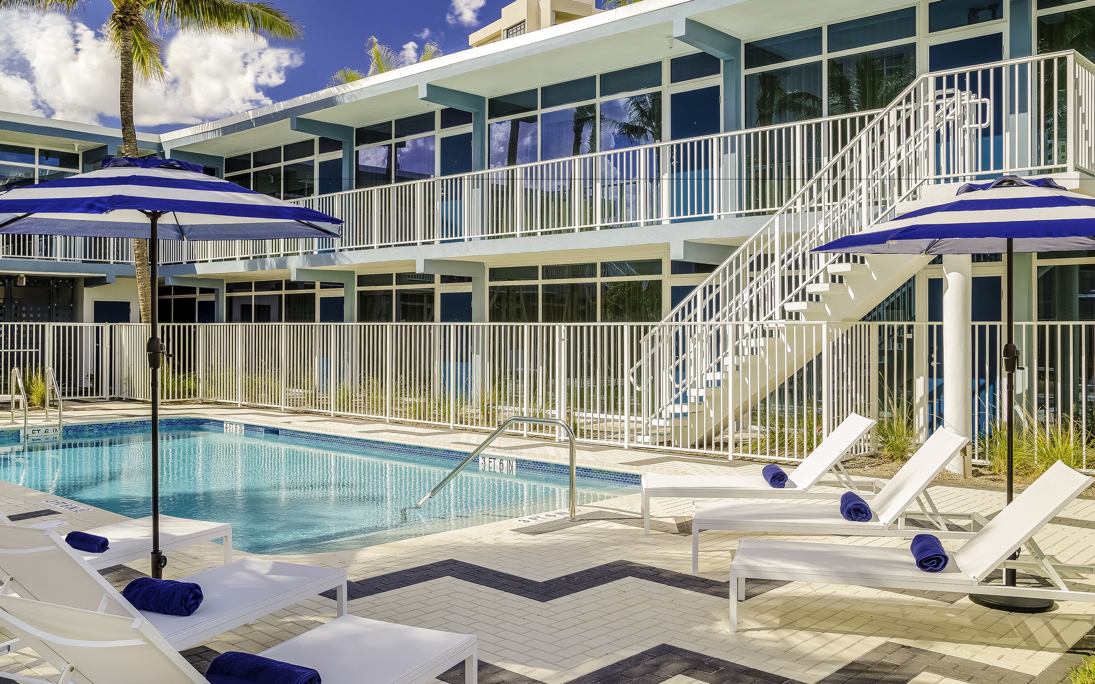 A pool area with lounge chairs and umbrellas, a staircase, and a building with large windows.