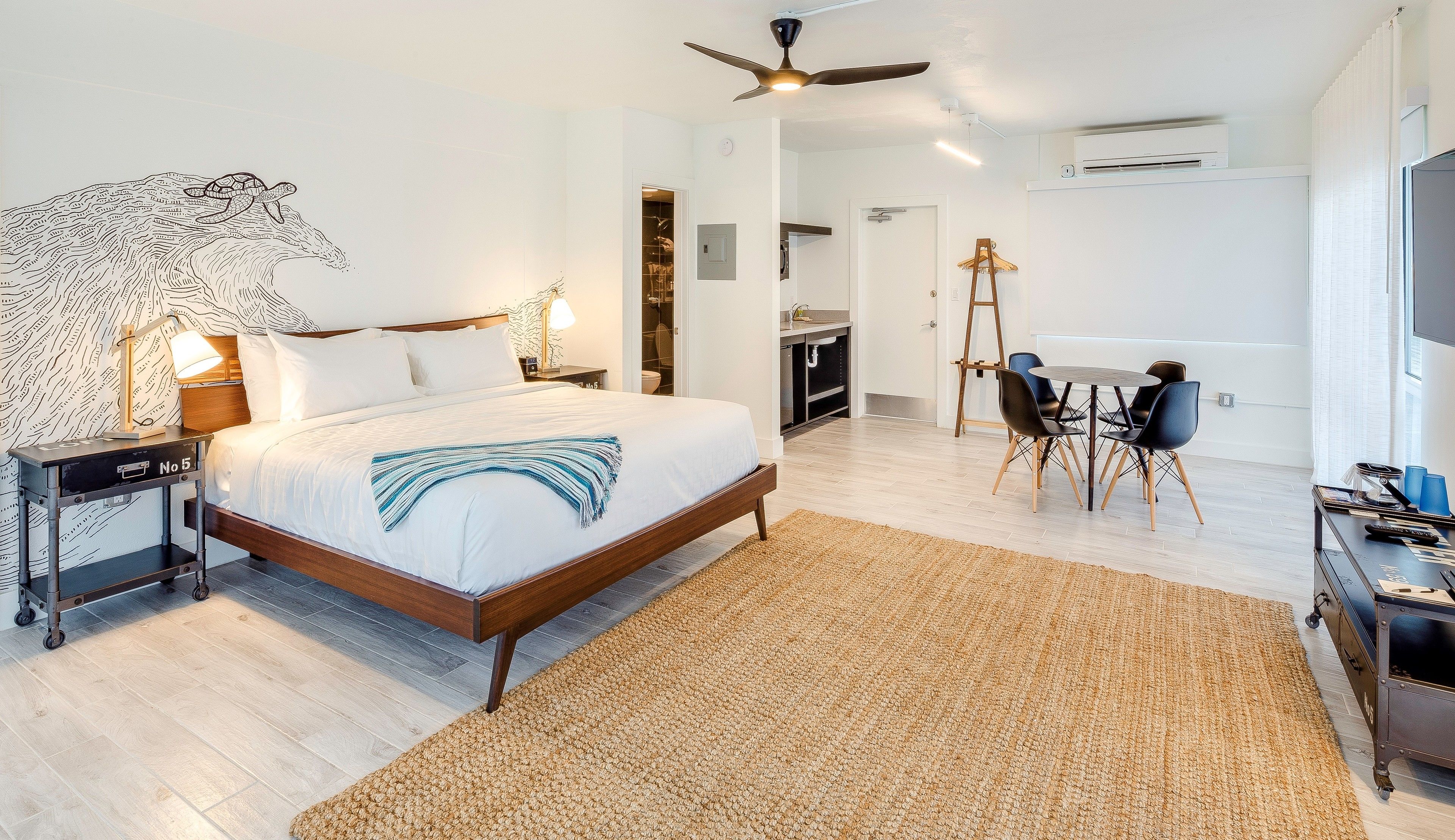 Quarto de hotel moderno com uma cama grande, uma escrivaninha, uma cadeira e um ventilador de teto.