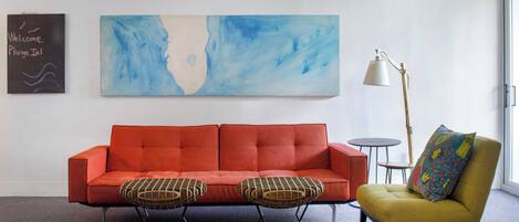 A room with a red sofa, two armchairs, a floor lamp, and a large abstract painting.