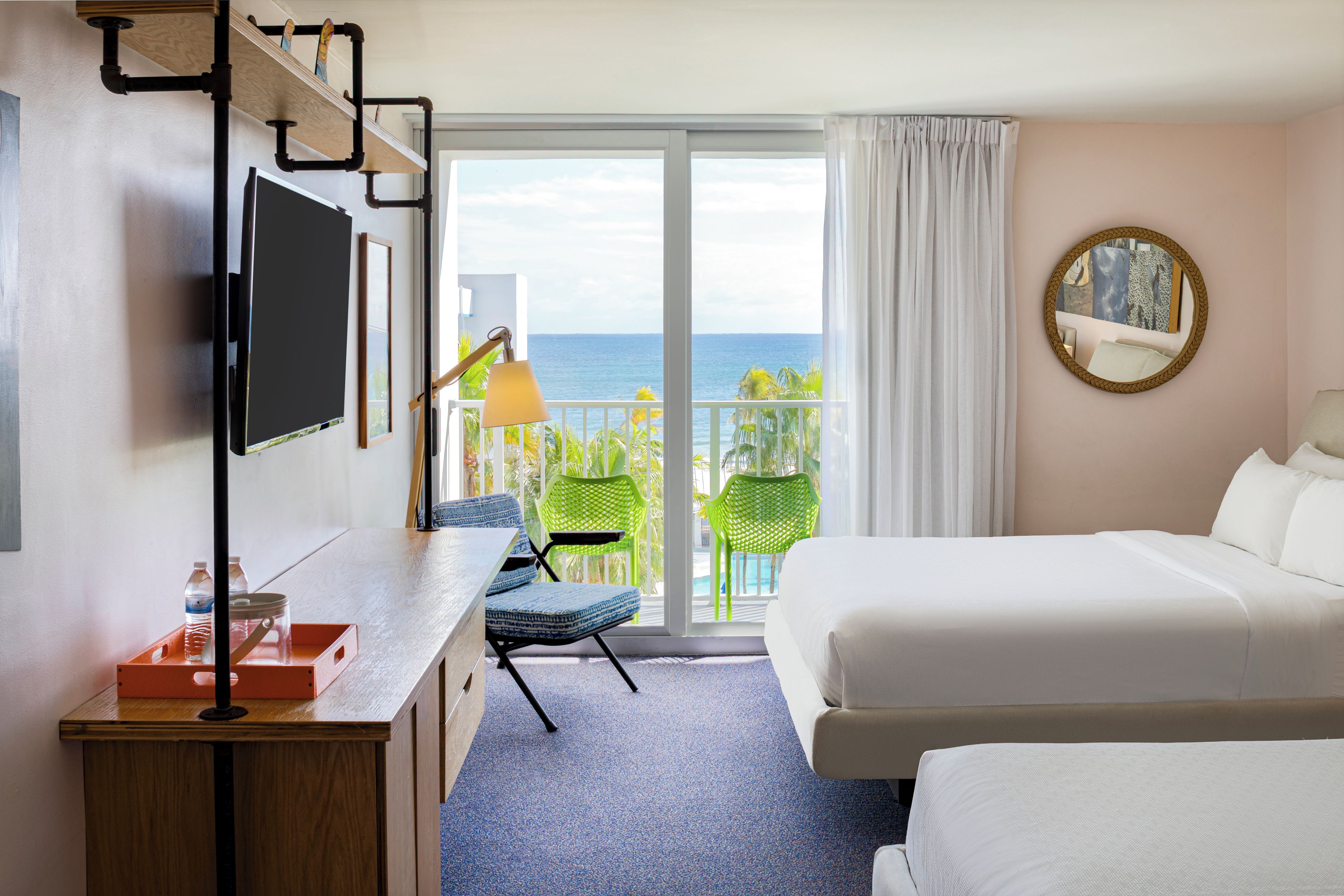 Habitación de hotel con una cama, un escritorio con televisor, una silla y vista al océano.