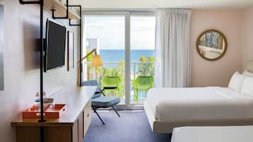 A hotel room with a bed, a desk with a TV, a chair, and a view of the ocean.