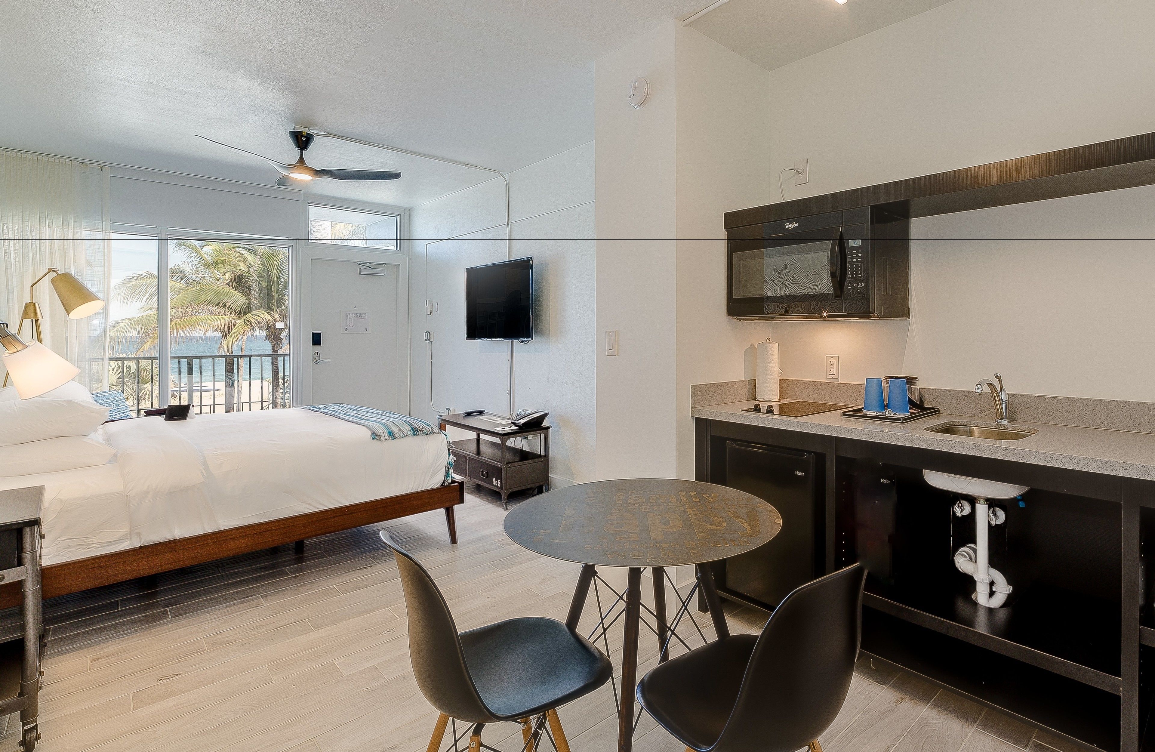 A modern hotel room with a bed, a desk, a round table, and a kitchenette.