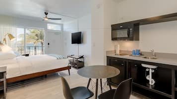 A modern hotel room with a bed, a desk, a round table, and a kitchenette.