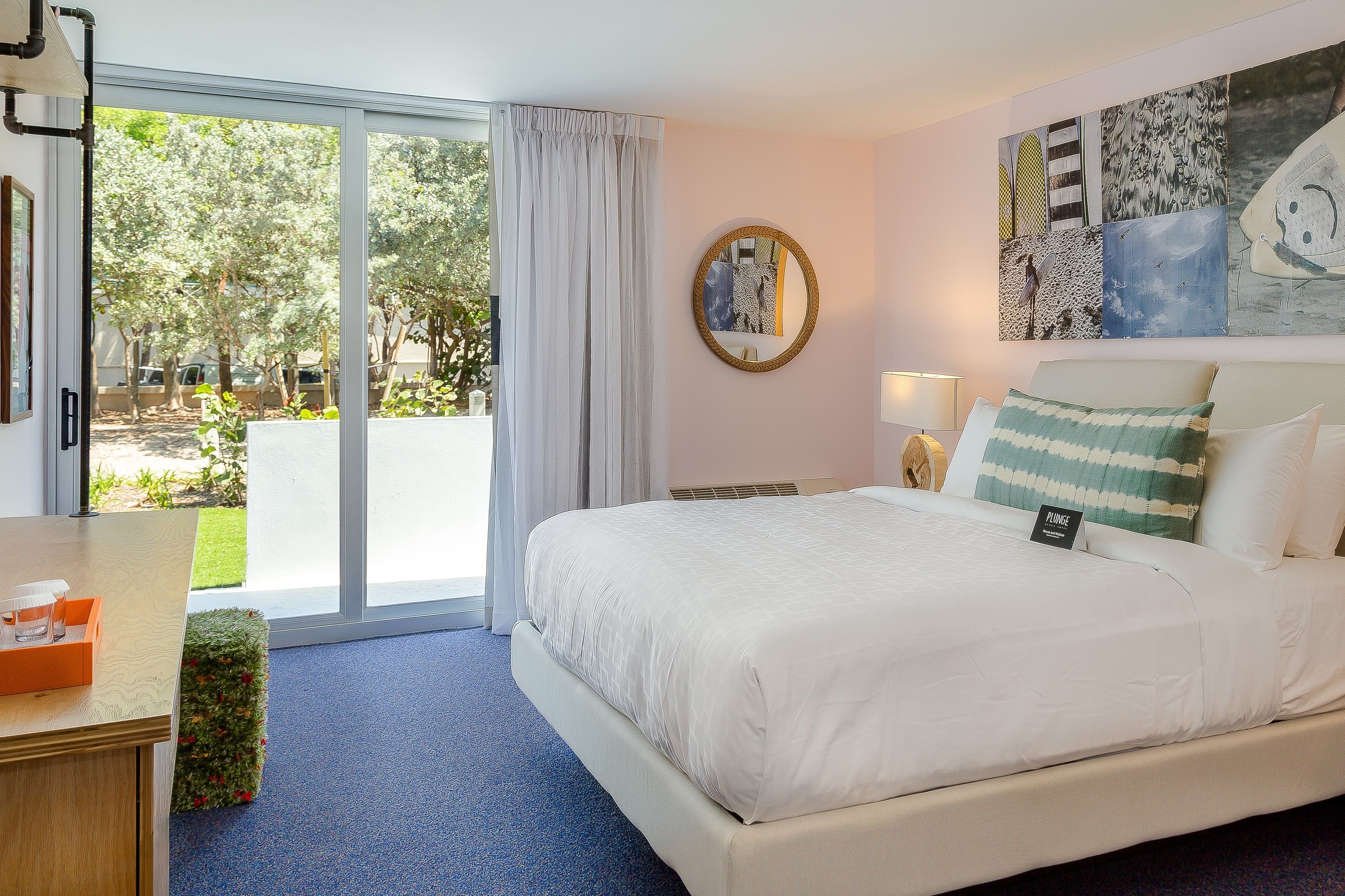 A hotel room with a large bed, a sliding glass door to the outside, a round mirror on the wall, and a small table with a tray.