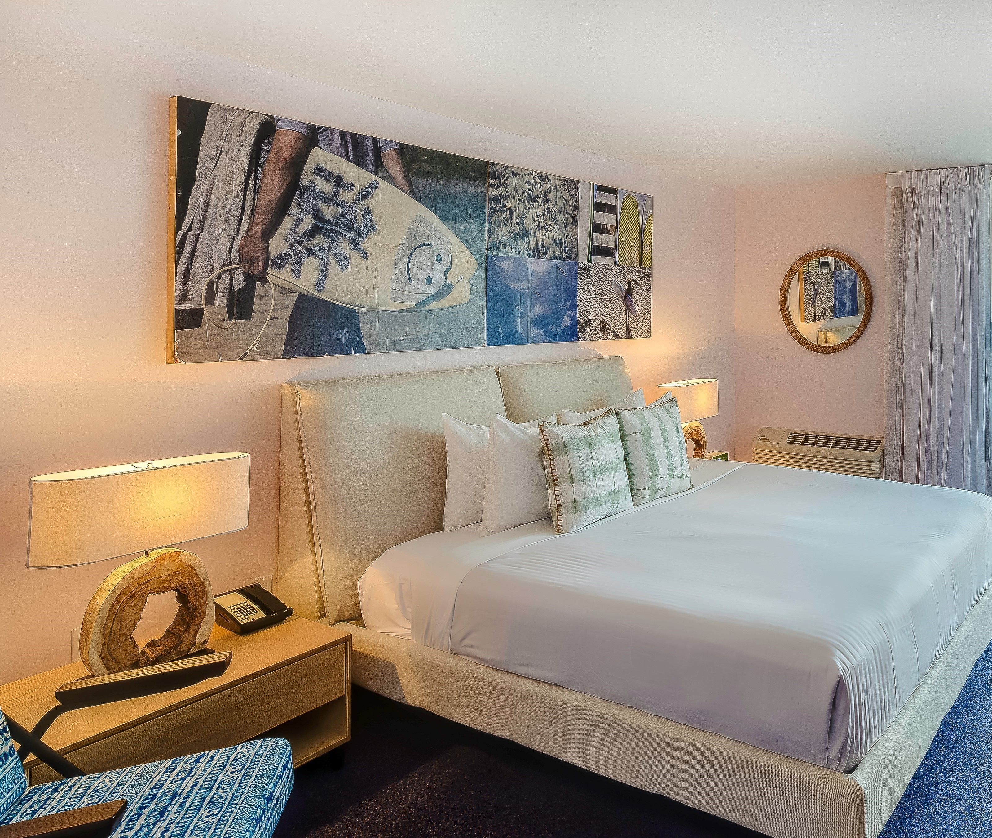 A hotel room with a large bed, two bedside tables with lamps, a decorative mirror, and a wall art piece.
