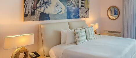Una habitación de hotel con una cama grande, dos mesitas de noche con lámparas, un espejo decorativo y una obra de arte en la pared.