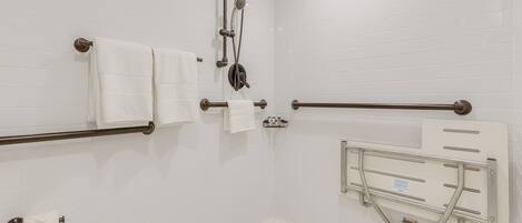 A modern bathroom with white subway tiles, a shower with a handheld showerhead, a grab bar, and a toilet paper holder.