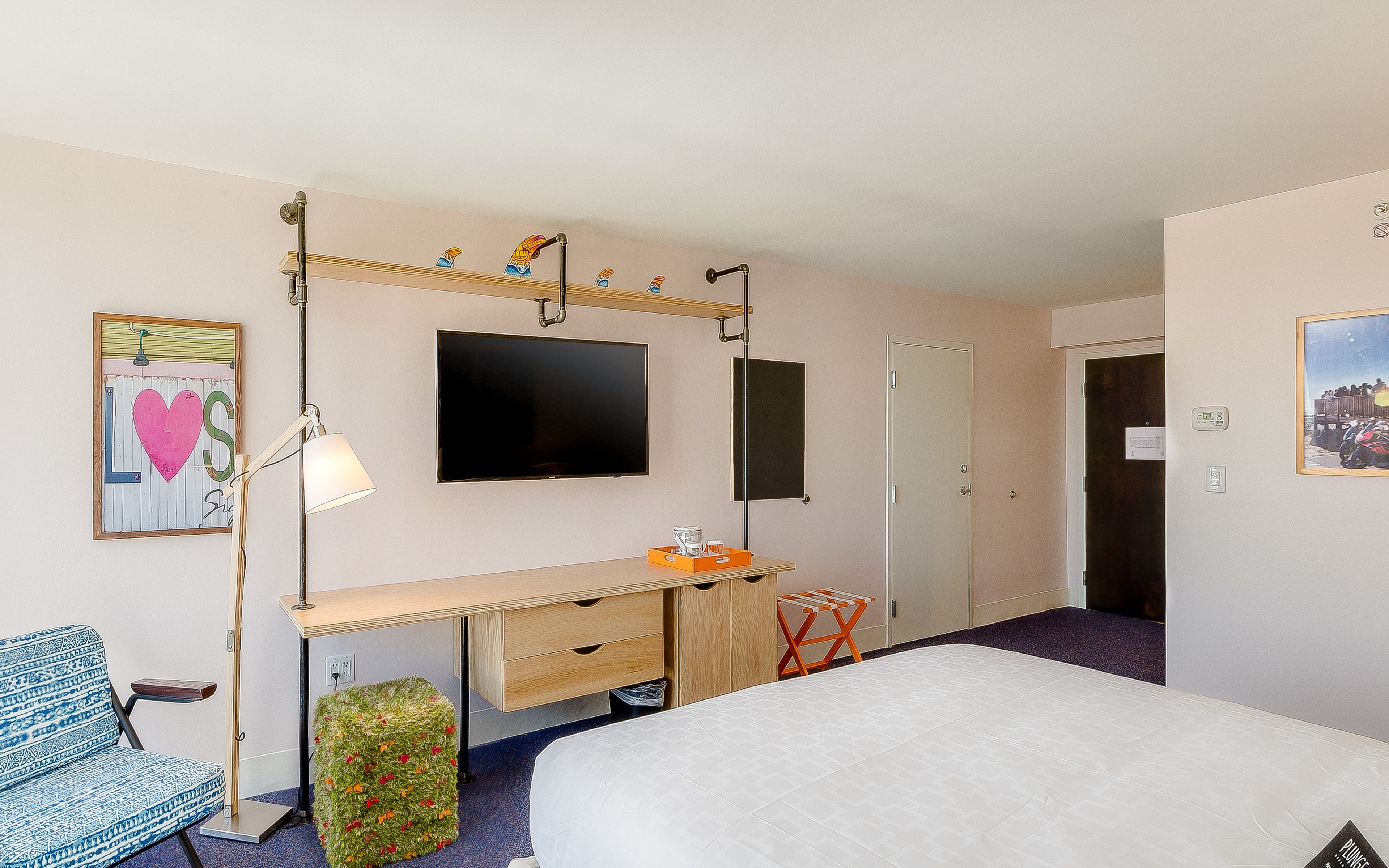A hotel room with a bed, a desk, a television, and a door.