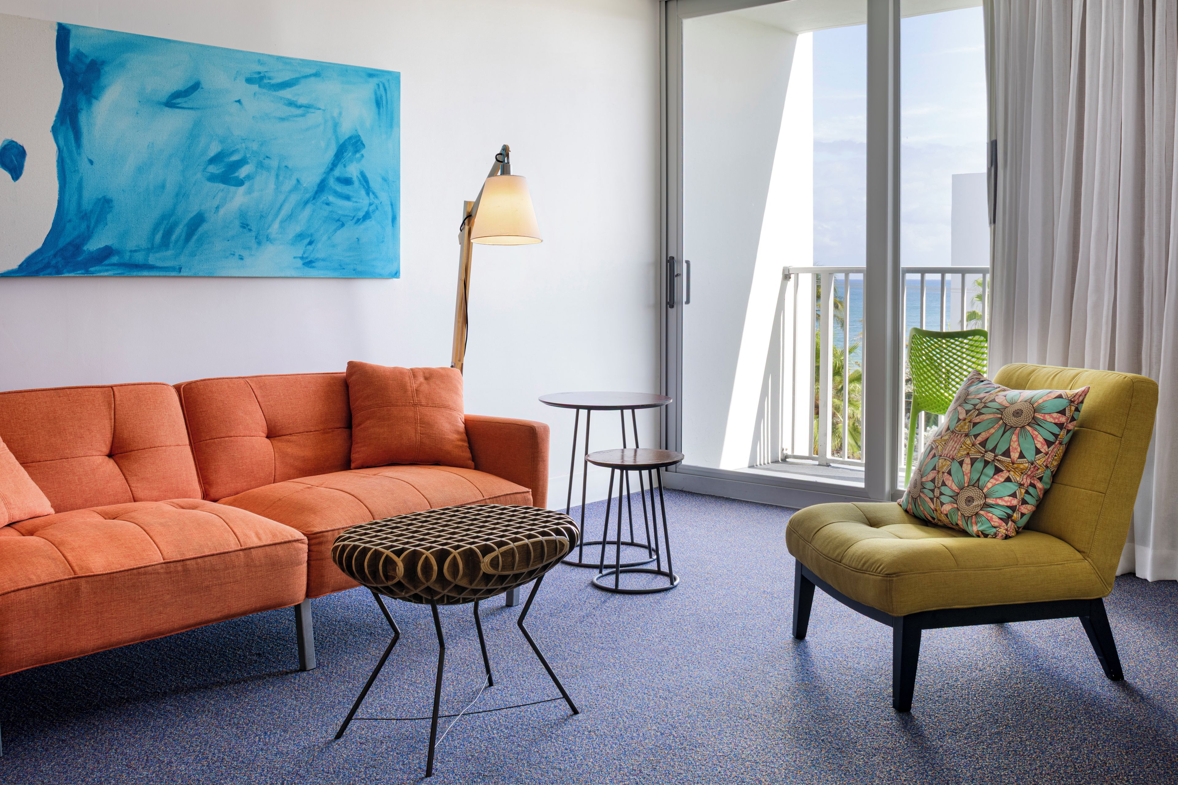 A room with a sofa, a chair, a small table, a lamp, and a view of the ocean through large windows.