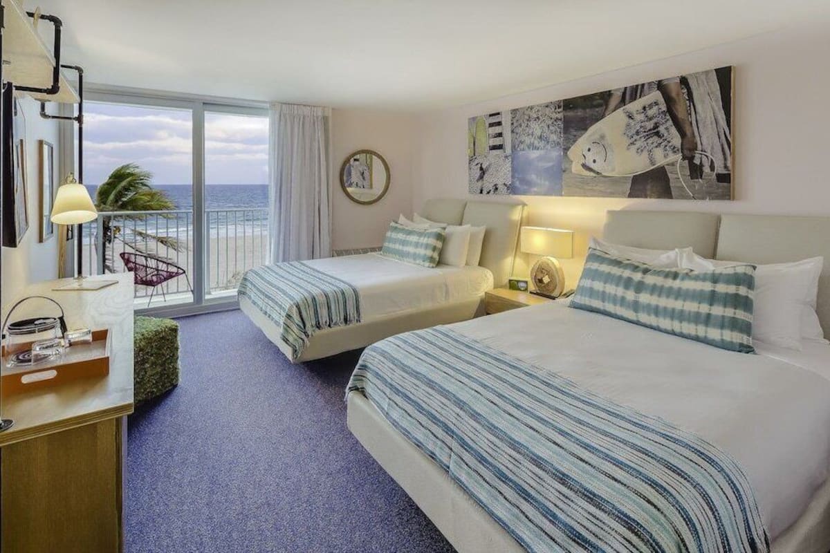 Habitación de hotel con dos camas, un escritorio, una silla y vista al océano.