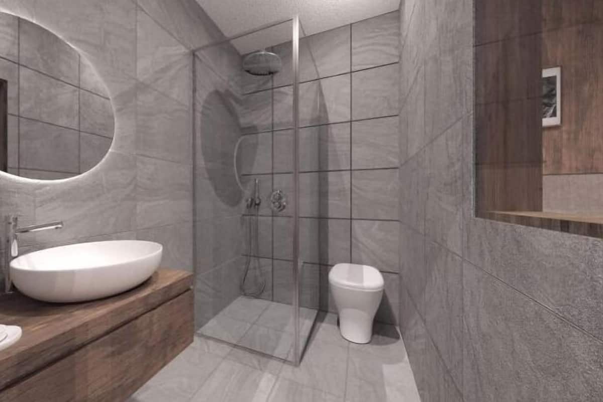 A modern bathroom with a round mirror, a wooden vanity, a white sink, and a glass-enclosed shower.