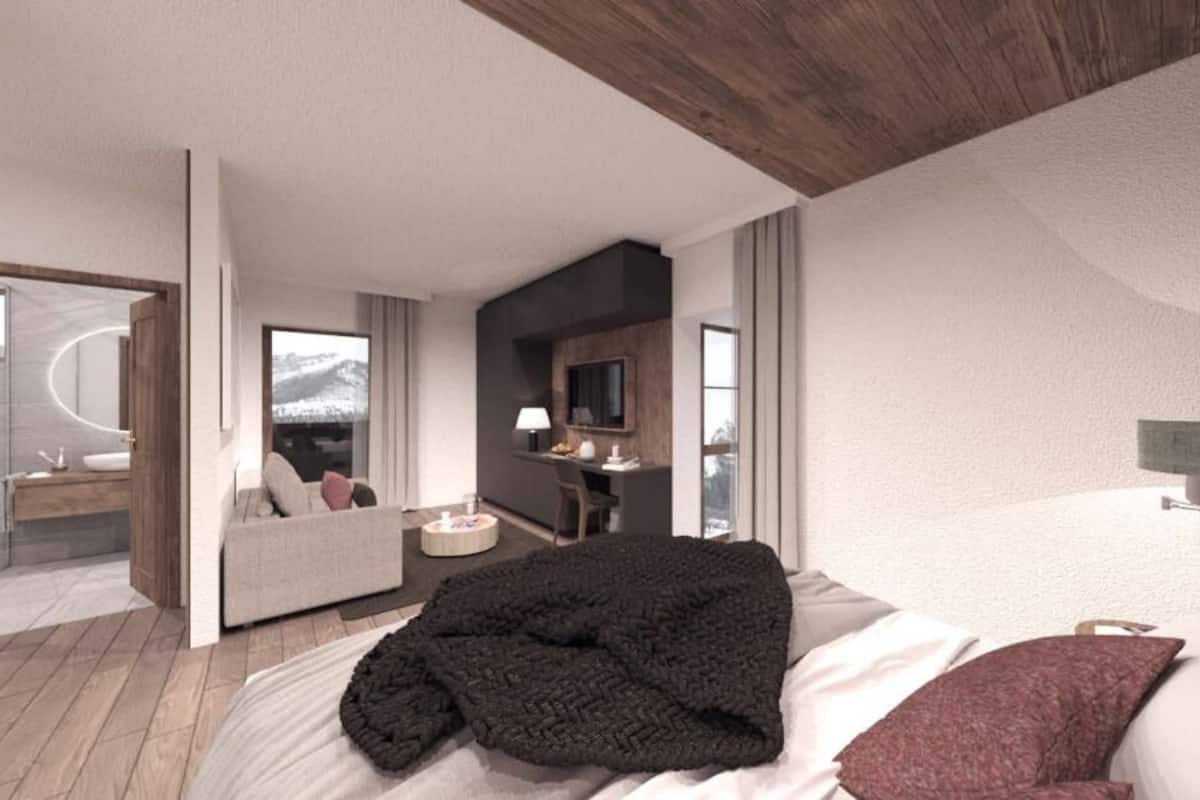 A modern hotel room with a large bed, a sofa, a desk, and a bathroom visible through an open door.