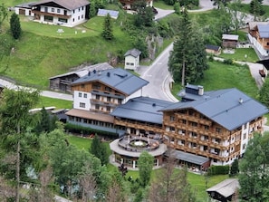 A multi-story hotel with a central courtyard, surrounded by lush greenery and a winding road. - Hotel Kärntnerhof (Heiligenblut)