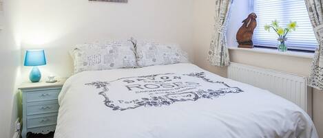 Una camera da letto con un letto, un comodino, una lampada, una finestra con tende e un elemento decorativo sul davanzale.