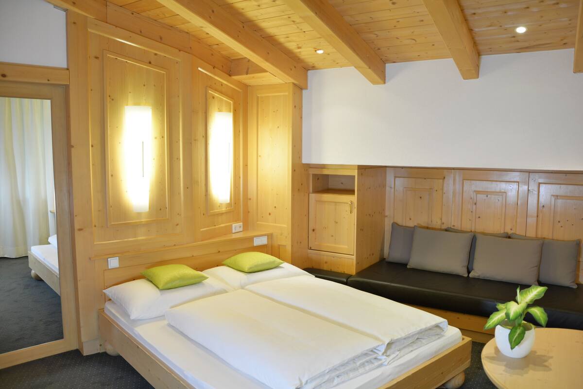 Una habitación de madera con dos camas, un banco y una pequeña mesa con una planta.