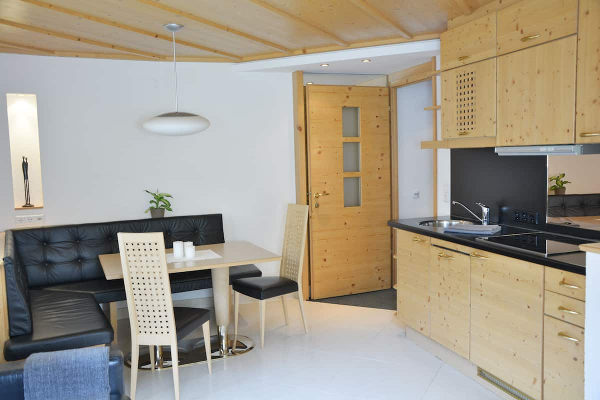 Una cocina moderna con armarios de madera, una zona de comedor con sofá de cuero negro, una mesa y sillas.