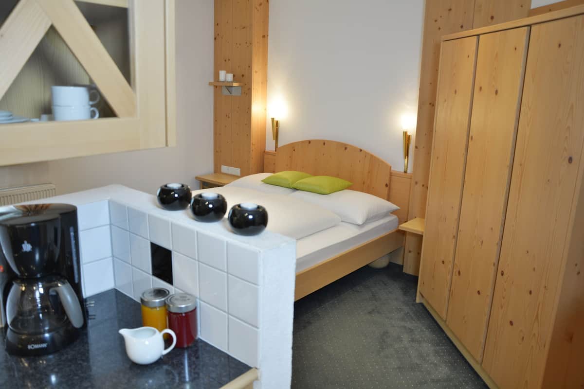 Una habitación con cama, armario de madera, una mesita con cafetera y un mueble con tazas.