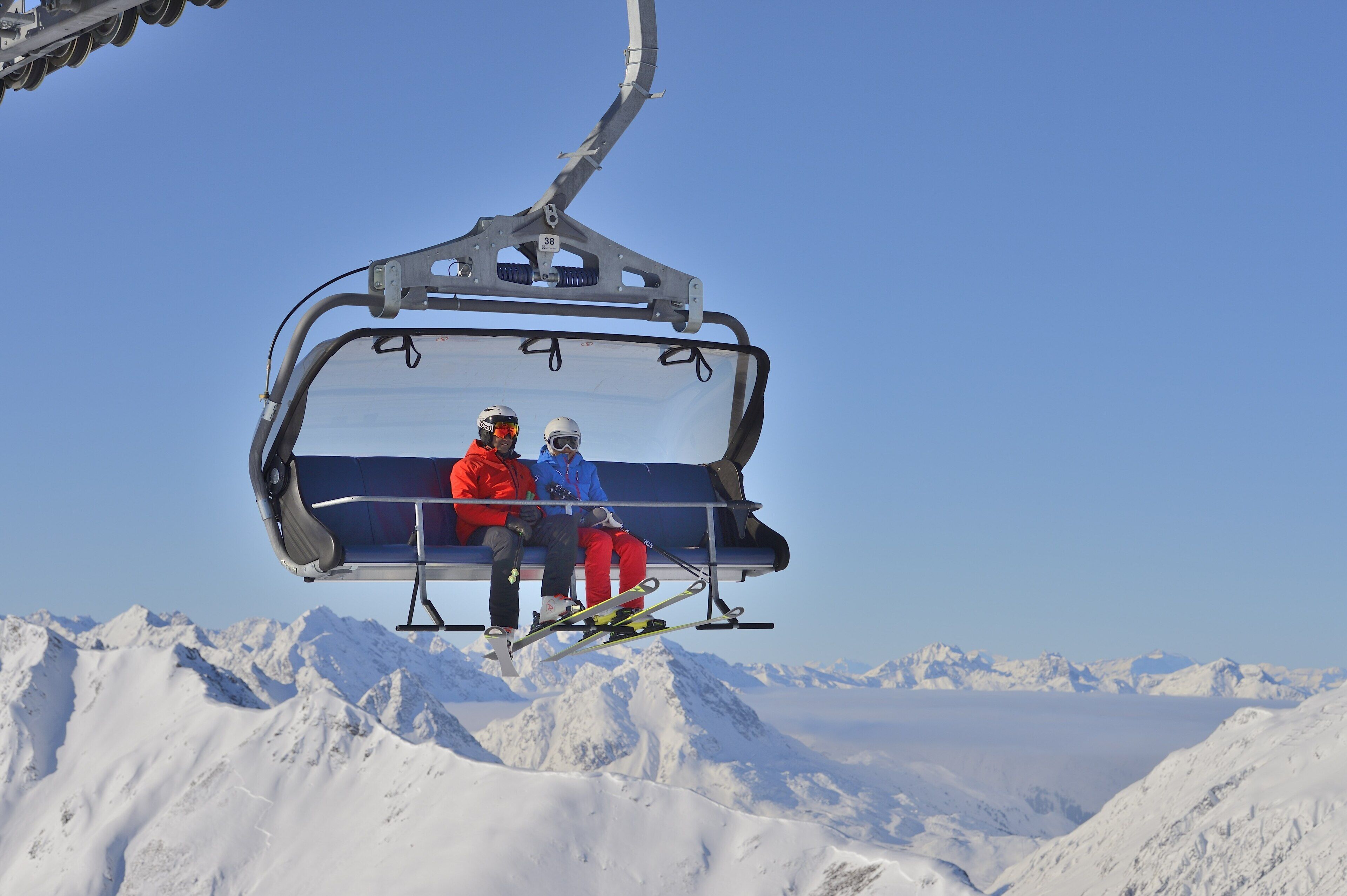 Een skilift met twee personen, omringd door met sneeuw bedekte bergen.
