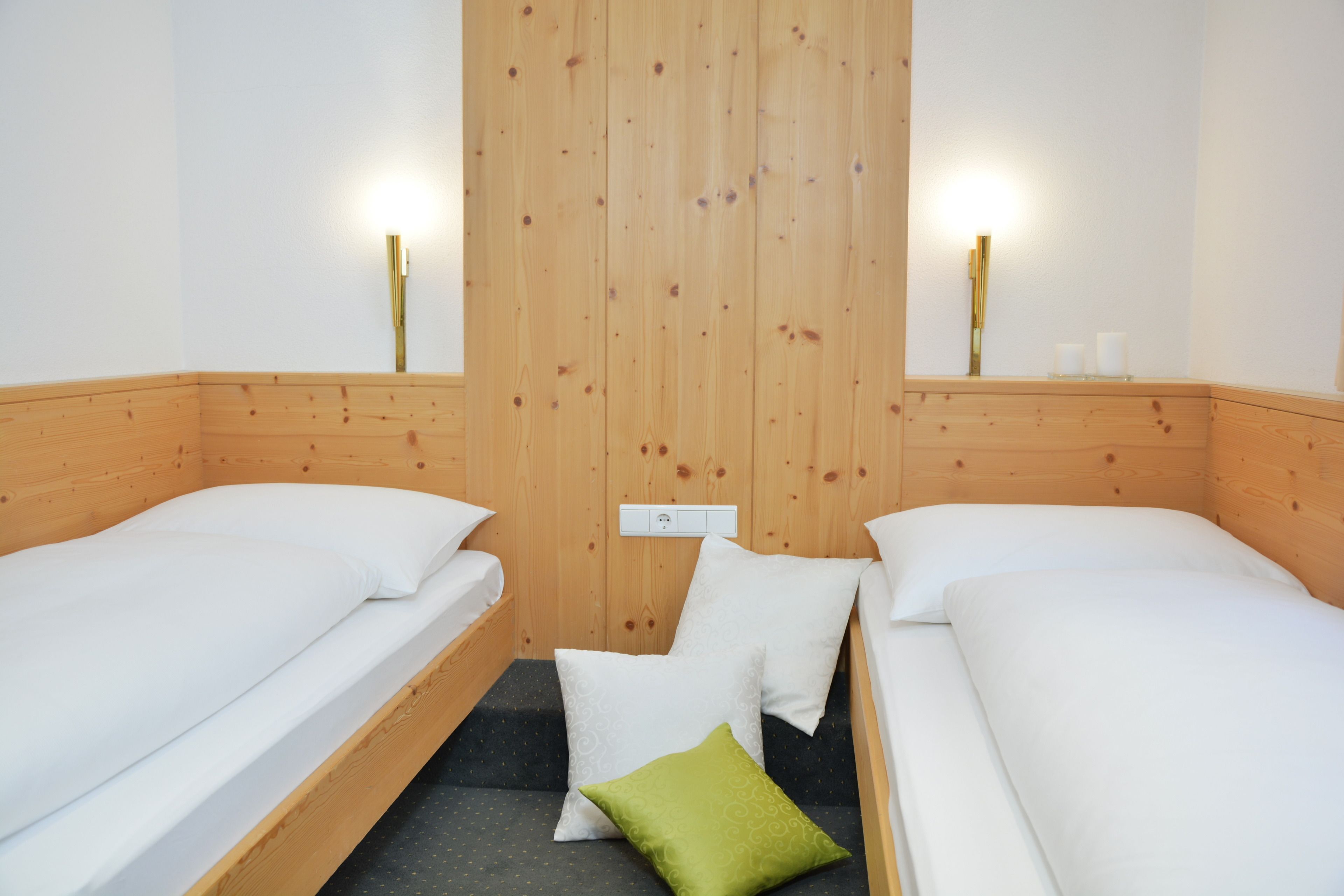 A room with two single beds, wooden headboards, a small seating area, and wall-mounted lights.