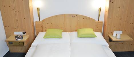 Un lit double avec deux oreillers, une tête de lit en bois, des tables de chevet avec des lampes, et une petite table de chevet avec un livre et un verre de vin.