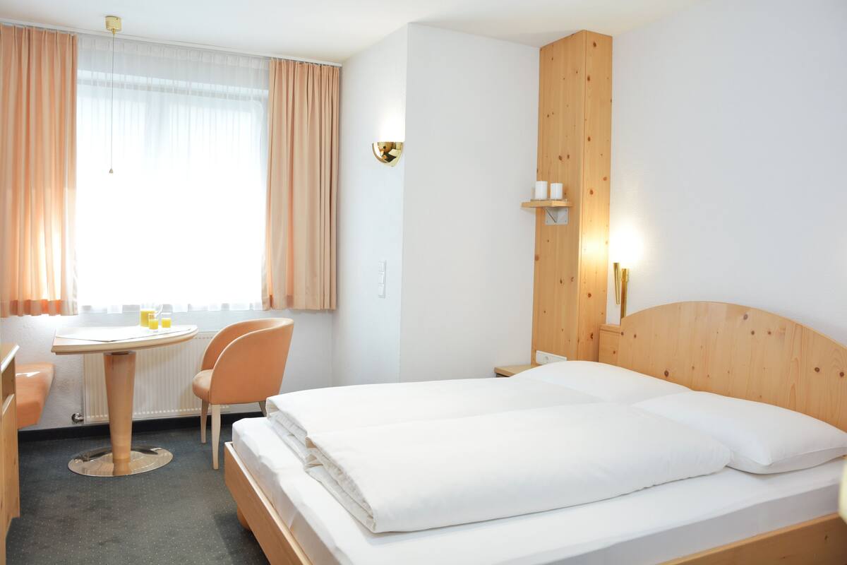 Una habitación de hotel con cama, escritorio, silla y ventana con cortinas.