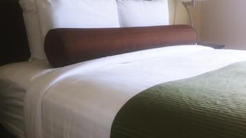 Un letto rifatto con lenzuola bianche, una testata marrone e una coperta decorativa verde.