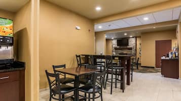 A dining area with a stone fireplace, a self-service beverage station, and a kitchen area.