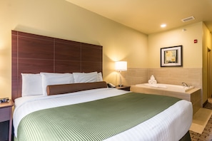Une chambre d’hôtel avec un grand lit, une table de chevet avec une lampe, une salle de bain avec une baignoire et un tableau encadré au mur.