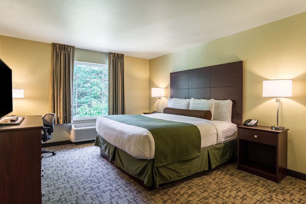 Ein Hotelzimmer mit einem großen Bett, zwei Nachttischlampen, einem Schreibtisch mit Stuhl und einem Vorhangfenster.