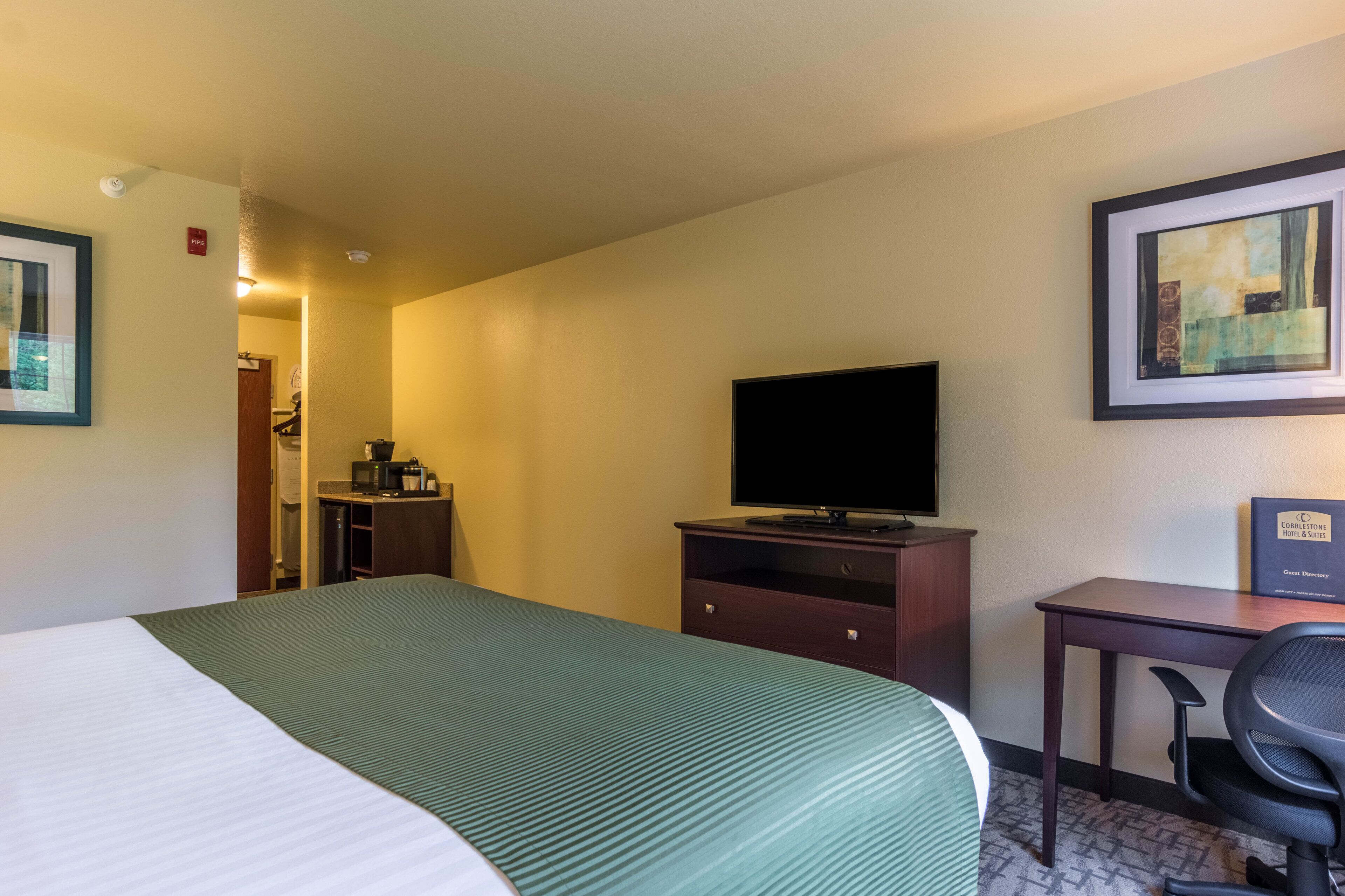 A hotel room with a bed, a desk, a chair, a television, and a framed picture on the wall.