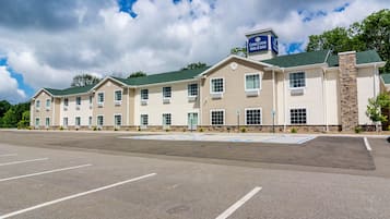 Hotel features a modern design with a flat roof and a prominent entrance, surrounded by a spacious parking area with designated handicapped parking.
