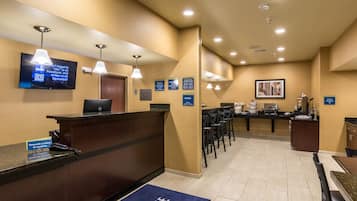 A hotel reception area with a reception desk, a television mounted on the wall, and a lounge area with chairs and tables.