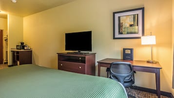 A hotel room with a bed, a desk, a chair, a television, a lamp, and a framed picture on the wall.