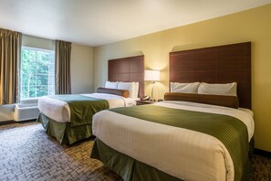 Une chambre d’hôtel avec deux lits, une grande fenêtre avec des rideaux, une lampe de chevet et un téléphone fixé au mur.