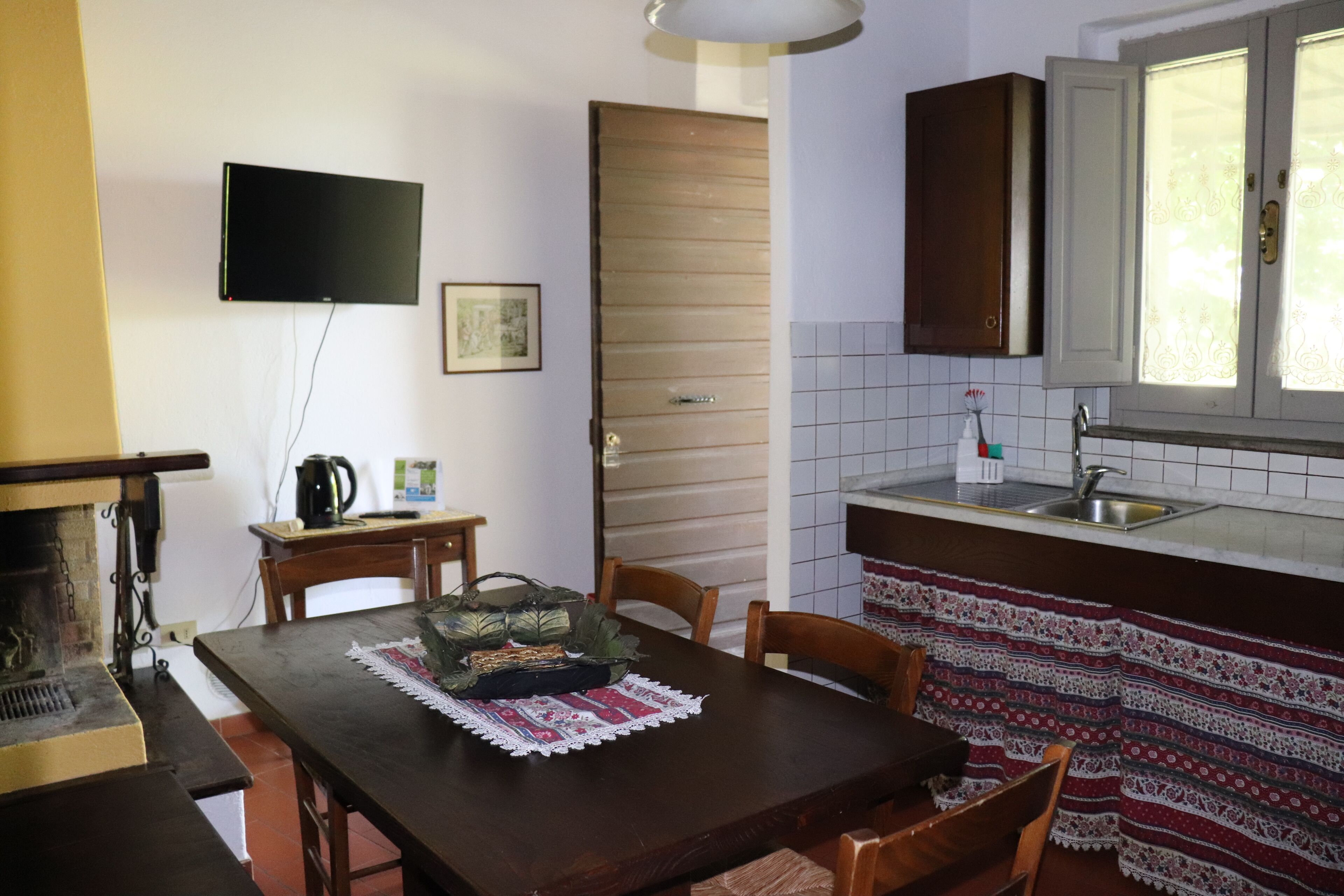 A compact kitchen with a wooden table, chairs, a television, and a tiled backsplash.
