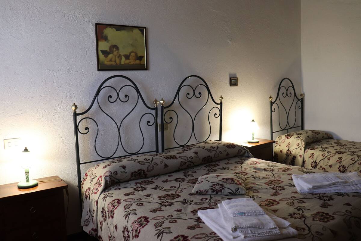 A bedroom with a metal headboard, floral bedding, a bedside lamp, and a framed picture on the wall.