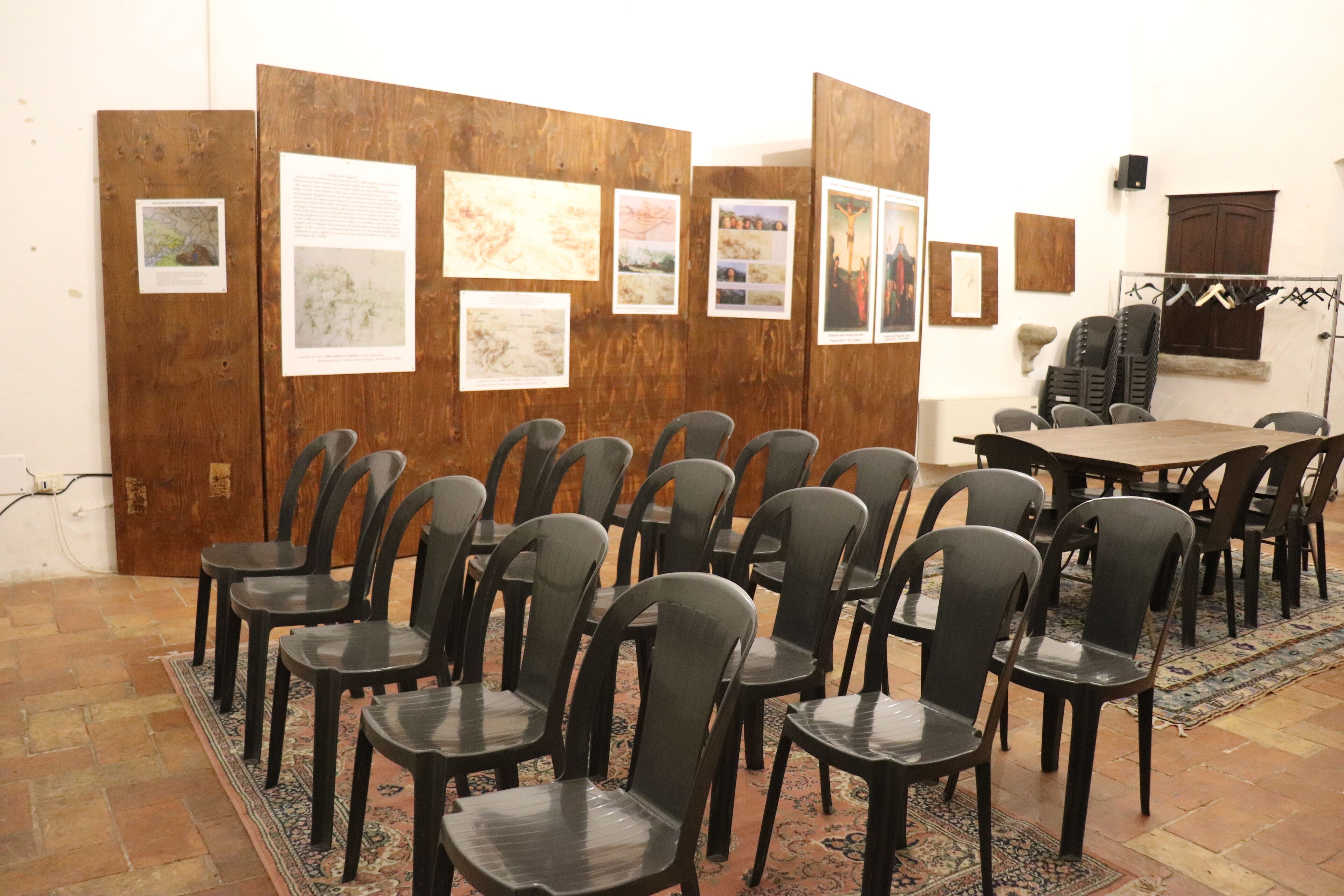 A conference room with rows of chairs, a wooden partition with framed pictures, and a table with chairs.