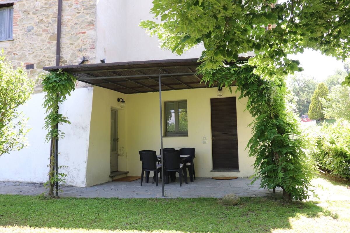 An outdoor patio with a table and chairs, a covered area, and a stone building in the background.